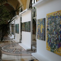 Paintings of bright flowers in an exhibition, with a palm tree in the forground